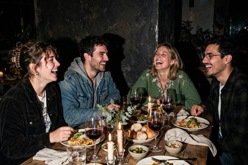 A candid flash photo at a dinner party: friends laughing around a long table with candles and wine glasses, harsh direct flash, deep shadows behind them, a 2000s snapshot feel, warm and fun.
