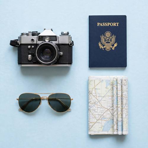 Flat lay of travel essentials on a soft blue background, camera, passport, sunglasses and map, bright even light, knolling style