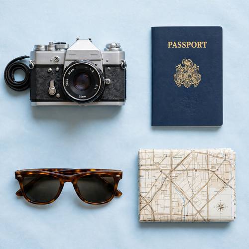 Flat lay of travel essentials on a soft blue background, camera, passport, sunglasses and map, bright even light, knolling style